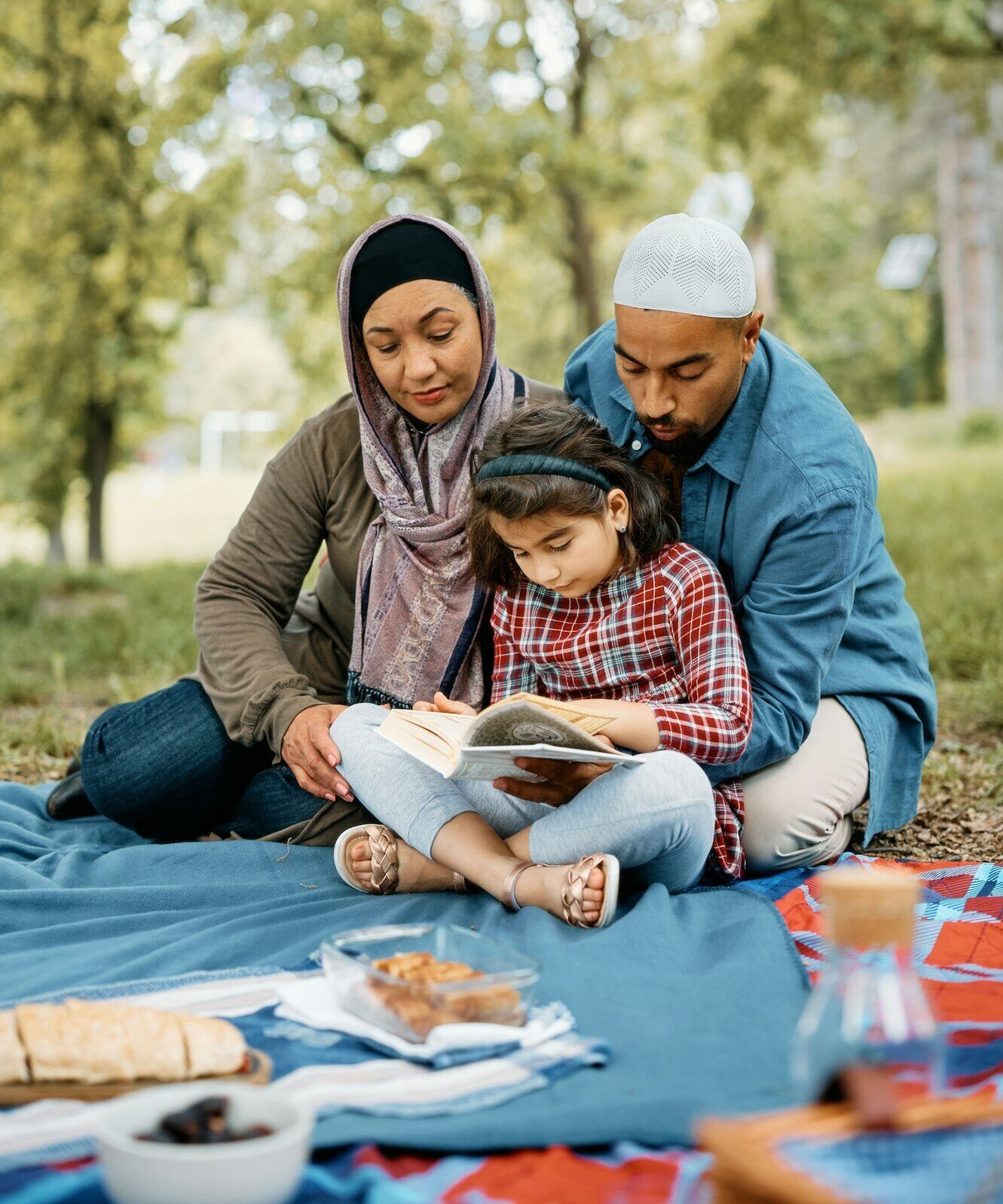 Muslim family reading Koran during their picnic day in nature.