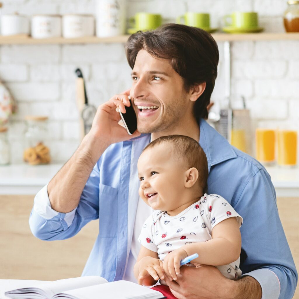 Young man talking on phone at home office and take care of baby